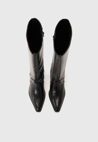 Bottes noires en cuir à bout pointu, arrivant au genou, avec une texture lisse et un léger détail de fronce en haut, comportant une fermeture éclair sur le côté.