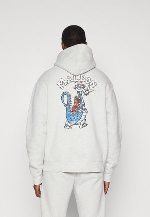 Grå sweatshirt med en stor färgglad tecknad drakgrafik på baksidan, med inslag av blått och rött. Designen inkluderar text ovanför grafiken.
