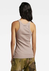 Top in tessuto a coste beige con scollatura rotonda, caratterizzato da un logo nero sul retro. Abbinato a pantaloni cargo con motivo camouflage.