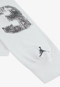 Valge pika varrukaga särk, mille ees on suur must grafikaarv ja varrukal must Jordan logo. Pehme puuvillane materjal.