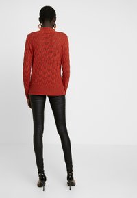 Röd stickad tröja med ett strukturerat mönster, långärmad och med ribbad nederkant. Kombinerad med svarta läderleggings och högklackade skor.