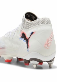 Weißer Fußballschuh mit strukturiertem Obermaterial, schwarzem Puma-Logo, roten und blauen Akzenten sowie konischen Stollen für Traktion auf Rasenflächen.