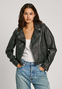 Zwarte leren motorjack met zilverkleurige hardware, een reverskraag, een ritssluiting aan de voorkant en een aansluitend ontwerp, in combinatie met lichtblauwe jeans.