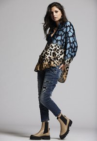 Flowing blue and black blouse with leopard print, paired with distressed blue jeans and beige ankle boots with black accents, creating a layered look.