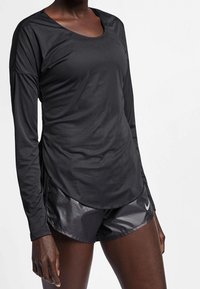 Svart långärmad träningsöverdel i slät tyg, med rundad halsringning och sidoknapp, tillsammans med svarta shorts som har en logotyp.