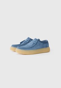Blue suede shoes with a rounded toe, featuring double stitching and a rubber sole with ridges. Lace-up design and minimal detailing.