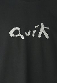 Svart bomullströja med ett stort, oregelbundet vitt tryck av ordet "Quik" i en lekfull, abstrakt typsnittsstil.