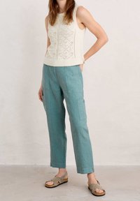Knit sleeveless top in cream with textured diamond patterns, paired with loose teal linen pants featuring side pockets and a relaxed fit.