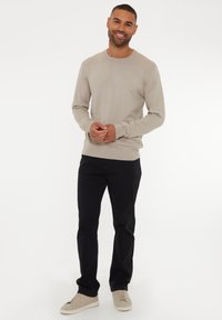 Maglione lavorato a maglia beige con scollatura rotonda, polsini e orlo aderenti, abbinato a pantaloni neri e sneakers grigie chiare. Design semplice, texture liscia.