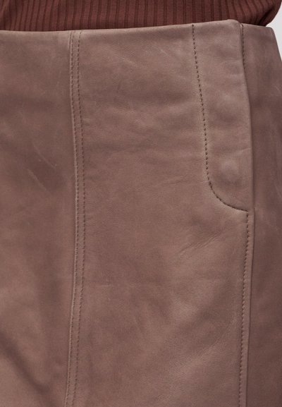 Κοντινό πλάνο μιας απαλής καφέ φούστας από σουέντ με κατακόρυφες ραφές και πλαϊνή τσέπη, φορεμένη με ριμπ πλεκτό σκούρο κόκκινο τοπ.