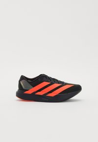 Black athletic shoe with neon orange stripes, mesh detailing on the upper, and a textured sole. Features a sleek design with minimal accents.