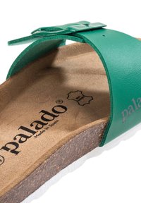 Sandalia deslizante de cuero verde con una plantilla plana de corcho, suela de goma blanca y correa ajustable que presenta una hebilla brillante. Marcada "palado" en el interior.
