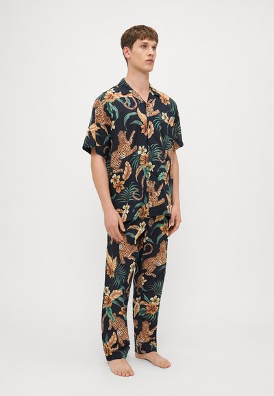 Set de pijamale cu mânecă scurtă în albastru închis, cu un imprimeu floral și animalier, având lei, frunze tropicale și flori de hibiscus.