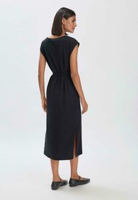 Musta midi-mekko, jossa on hihattomat hihat, vyötärövyö ja sivuaukot. Sileä kangas ja yksinkertainen muotoilu korostavat minimalismia ja eleganssia.