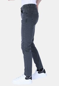 Grijze slim-fit jeans met subtiele slijtage, vijf zakken en een zachte textuur, gecombineerd met wit-zwartige sneakers.
