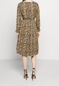 Vestido de manga larga con estampado de leopardo en tono marrón con manchas negras, cintura ceñida, falda con pliegues y mangas recogidas. Llevado con tacones negros de tiras.