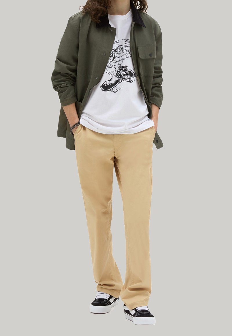 Camicia verde oliva con bottoni, t-shirt bianca con stampa grafica, pantaloni beige, sneakers nero e bianco. Il tessuto sembra liscio; il design presenta una stampa grafica.
