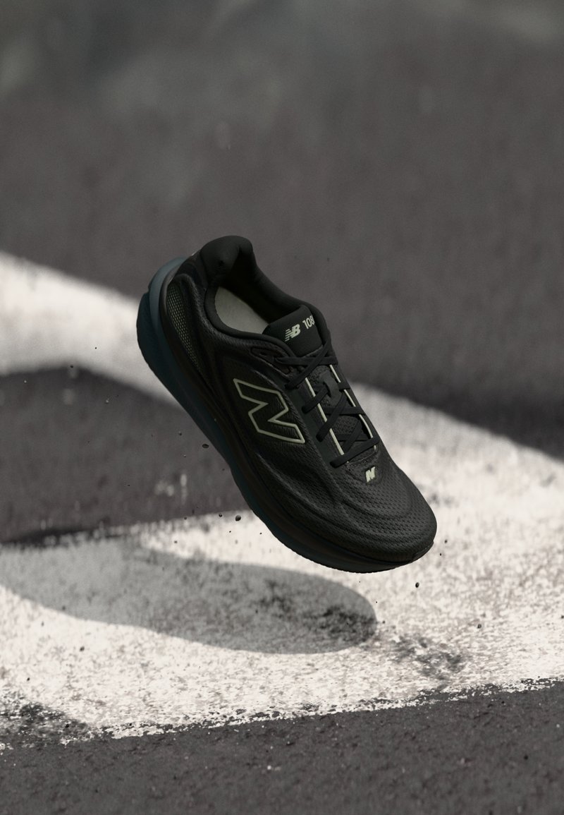 Μαύρο αθλητικό παπούτσι με επάνω μέρος από δίχτυ, σόλα από αφρό και αντανακλαστικές λεπτομέρειες. Διαθέτει επίπεδα κορδόνια και μαλακό γιακά, αιωρούμενο πάνω από πίστα αγώνων.