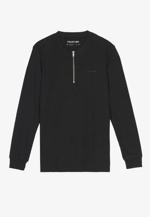 Chemise noire à manches longues avec un col haut, fermeture éclair frontale quart, texture côtelée et logo discret au niveau de la poitrine.