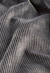 Tissu côtelé gris doux avec des lignes texturées verticales et des plis doux créant des contrastes de lumière et d'ombre.