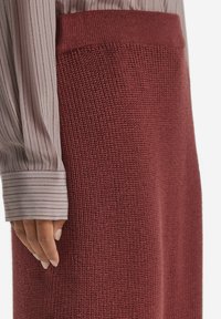 Stickad burgundy kjol med texturerad tyg, med hög midja och rak silhuett. Matchad med en randig blus med långa ärmar.