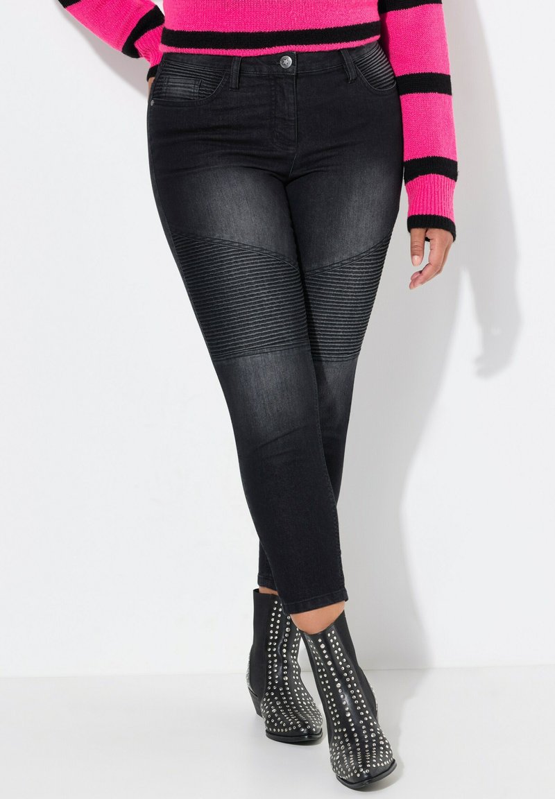 Jeans de mezclilla negra con acentos de textura acanalada, forma ajustada y cintura de altura media, combinados con botas de tobillo negras con tachuelas.