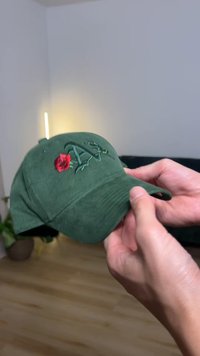 Πράσινο καπελάκι από κορδόνι με κεντητό κόκκινο τριαντάφυλλο και στιλιζαρισμένα γράμματα. Καμπυλωτό γείσο και ρυθμιζόμενη πίσω πλευρά για καλύτερη εφαρμογή.