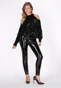Melnas plecu atbrīvojošas svīteri ar sekvīnēm un frēzēm, apvienots ar spīdīgām melnām pielāgotām legingām un stiletto zābakiem. Visur gludas struktūras.