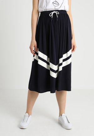 Marineblauwe plissé rok met een witte diagonale streepontwerp en een elastische tailleband, gedragen met witte sneakers. De stof is lichtgewicht.