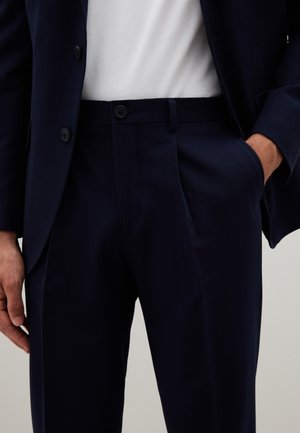 Marineblauwe pantalon met een platte voorkant, twee zijzakken en knoopsluiting. De stof lijkt glad met een subtiele textuur.