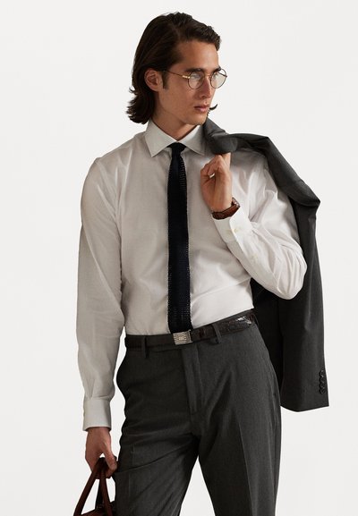 Valge pika varrukaga särk, mereväe stiilis tekstuurne lips, hall ülikonna jakk, mis on üle õla visatud, hall püksid, pruun vöö, ümmargused prillid, hoiab pruuni kotti.