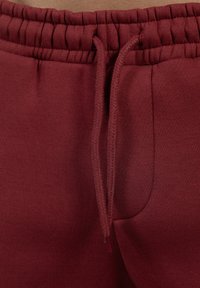 Bordeauxrode trainingsbroek met een elastische tailleband, voorzien van een trekkoord en een zachte textuur. Inclusief zijzakken en gladde naden.