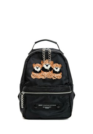 Persona que lleva chaqueta con capucha negra y pantalones con parches florales, llevando una mochila negra con diseño de flores y zapatos de plataforma beige.