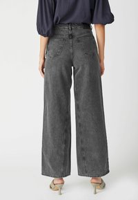 Jean noir à coupe large en denim, avec un design à cinq poches, taille haute et légères décolorations. Fini avec une texture lisse.