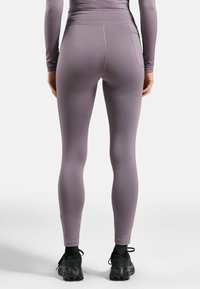 Paarse leggings met een hoge tailleband en glad, stretchy stof; achterzakdetails en een aangesloten ontwerp. G gedragen met gestructureerde zwarte sportschoenen.