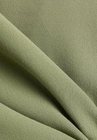 Tissu vert clair avec des plis doux et un motif texturé subtil créant une surface légèrement en relief et irrégulière.