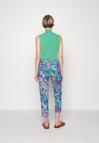 Groen geribbeld mouwloos top met een hoge halslijn, gecombineerd met kleurrijke, smalvallende broek met bloemenprint in roze, blauw en groen, gedragen met bruine sandalen.