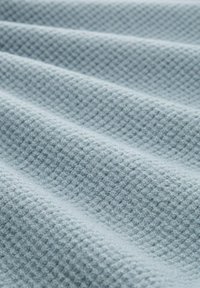 Teksturowana tkanina w jasnym niebieskim kolorze o wzorze waflowym, pokazująca złożone warstwy, które podkreślają miękki, pluszowy wygląd materiału.