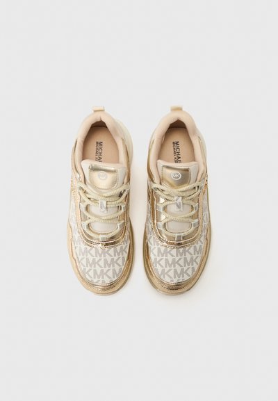 Zapatillas beige claro con acentos dorados, que presentan un upper estampado con el logo "MK", punta redonda y suela de goma plana. Los cordones son metálicos.