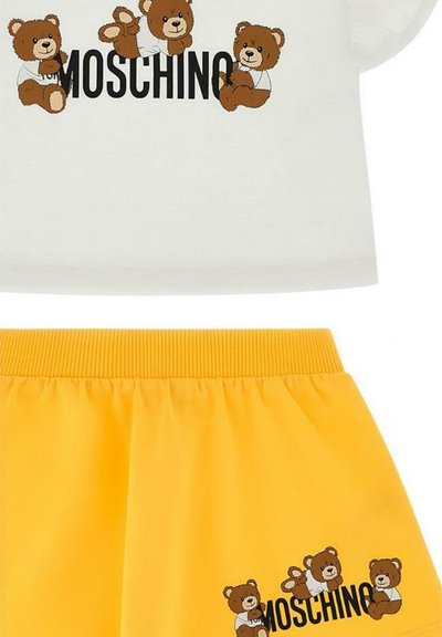 Weißes Baumwoll-T-Shirt mit drei Braunbär-Prints und "Moschino"-Logo; kombiniert mit einem gelben Rock mit elastischem Bund, der ein ähnliches Bärendesign aufweist.