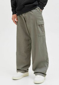 Olive green cargo nohavice so voľným strihom, bočnými vreckami a mäkkou, textúrovanou látkou. V kombinácii s bielymi teniskami.
