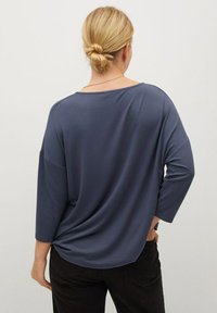 Top blu navy dalla vestibilità ampia, con maniche a tre quarti, scollatura ampia e texture liscia, abbinato a pantaloni neri. Design minimalista.