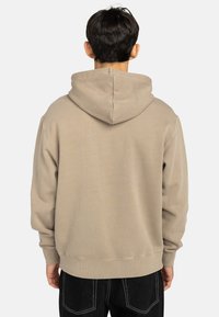 Beige hoodie med dragsko i huvan, ribbade muddändar och fåll. Mjuk textur, avslappnad passform och en minimal design som visar baksidan.