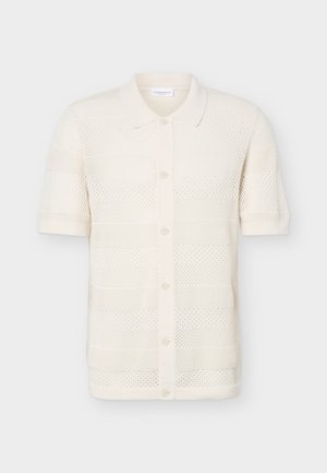 Μπλούζα σε κρεμ χρώμα, κοντά μανίκια, πλεκτή με γιακά και κουμπιά στο μπροστινό μέρος, με υφασμένο ανοιχτό σχέδιο και μονόχρωμη επένδυση στα μανίκια και το τελείωμα.