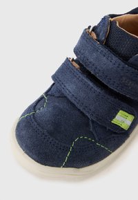 Navy blue suede toddler shoe with two Velcro straps, white rubber sole, green stitching details, and a reflective accent.
