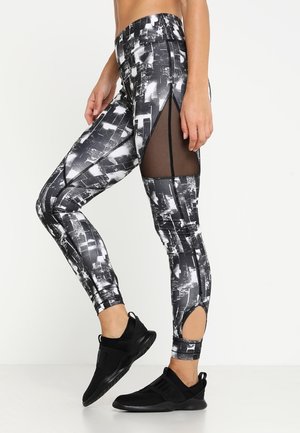 Leggings à motifs noir et blanc avec des découpes en maille sur les côtés et un design ajusté, associés à des chaussures de sport noires.