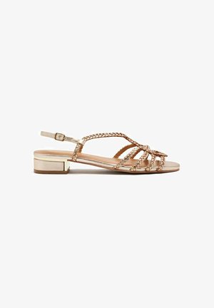 Sandali flat in rosé con cinturini intrecciati, fibbia regolabile alla caviglia e tacco basso. Superficie liscia e finitura metallica.