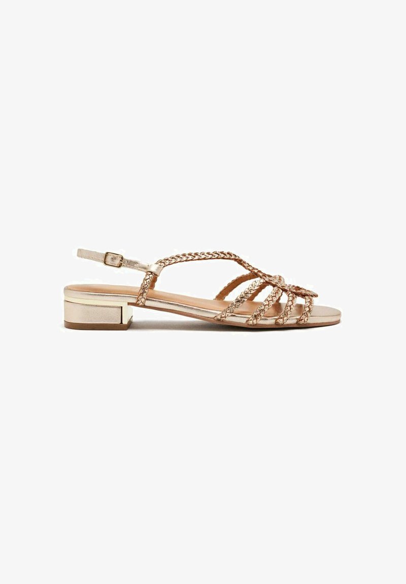 Sandalias planas de oro rosa con tiras trenzadas, hebilla ajustable en el tobillo y un tacón bajo. Textura suave y acabado metálico.