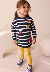 Striped navy and white knitted sweater with colorful appliqués, yellow leggings, and blue sneakers. Features playful designs and textures.