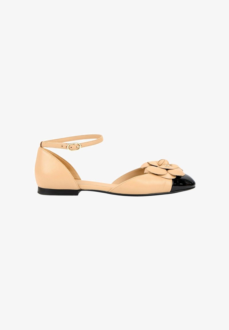 Chaussure plate beige avec bout rond noir, bride à la cheville avec boucle et fleur beige décorative sur la zone des orteils.